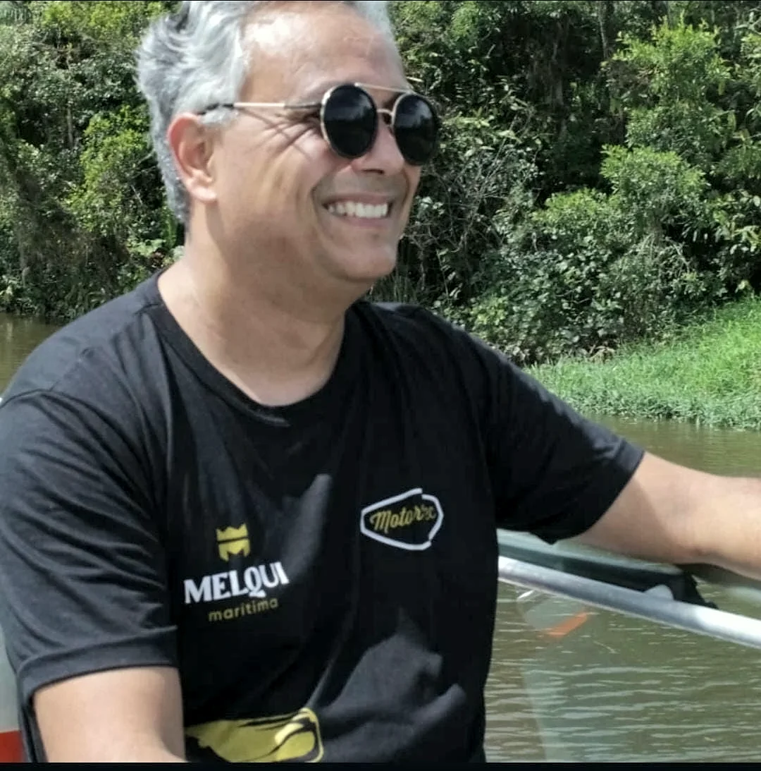 Marcel Segala sorrindo, de óculos escuros e camiseta da Melqui Marítima, a bordo de uma embarcação
